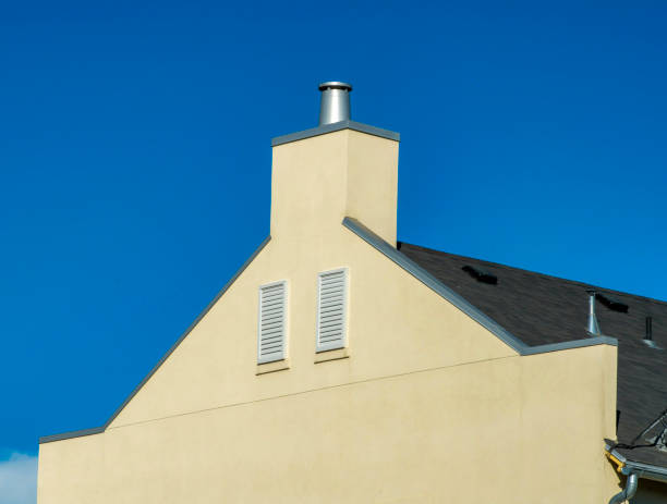 A rooftop of light yellow house with attic windows under the blue sky