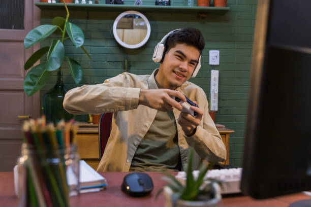 istock Young Hispanic male with headphones playing a computer game with a gamepad in his hands 1454780131