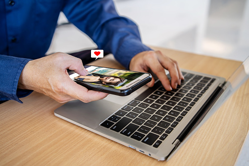 Man holding mobile phone, looking at attractive young woman's profile photo on dating app and pressing red heart like button.