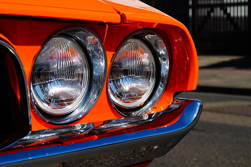 Front headlights of a Dodge Challenger RT, built in 1970. Detail of a beautifully renovated classic car, shining in the sun.