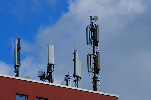 Mobile phone antennas of different providers on a house roof in Frankfurt, Germany. Blue cloudy sky.