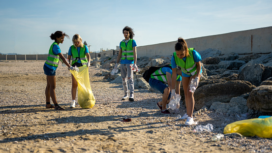 People cleaning up the beach, volunteers collecting the waste on the coast line, young students working in team aware of the pollution produced by the plastic industry