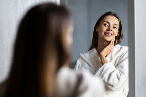 istock Young woman in bathrobe looking in bathroom mirror at home 1454788821