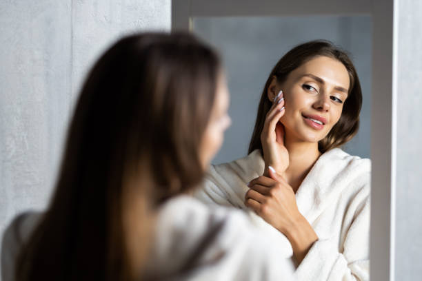 istock Young woman in bathrobe looking in bathroom mirror at home 1454788861