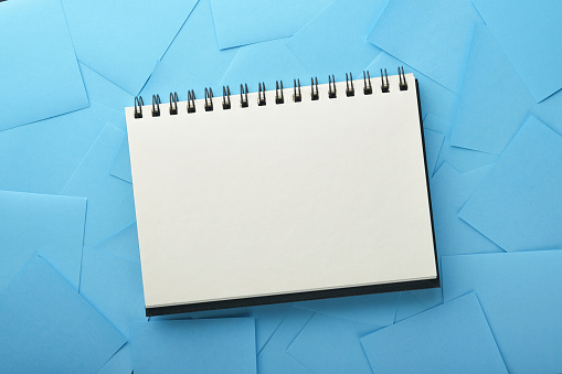 Blue paper stickers and notepad or book in middle on black background. Sticky notes blank with copy space ready for your message. New year goals or resolutions concept. Blue Monday idea. Mock up.