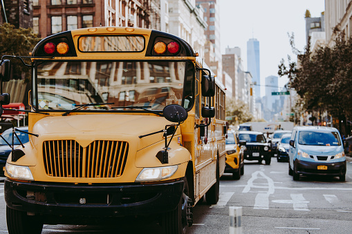 A typical yellow school bus on foreground and the WTC One World Trade Center on the background in Lower Manhattan.