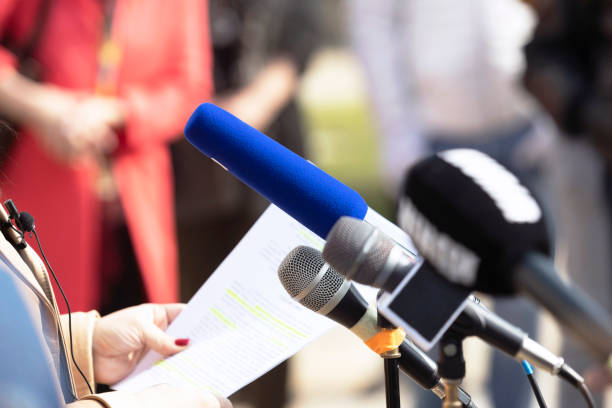 istock Whistleblower holding confidential document with highly classified information and giving a speech in front of microphones at press conference or news event 1454790935