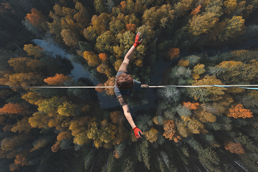 A breathtaking view of a tightrope walker walking along a line high above a beautiful forest. Topics of highline, longline, extreme activities. Top view.