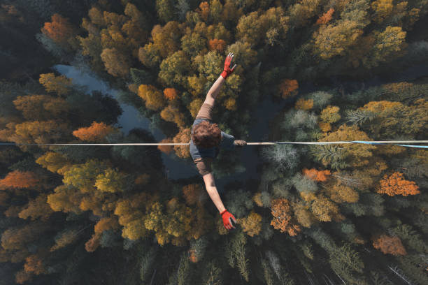 Highline over the forest. Rope walker walks on a rope at high altitude. Drone view. Slackline theme A breathtaking view of a tightrope walker walking along a line high above a beautiful forest. Topics of highline, longline, extreme activities. Top view. pace yourself photos stock pictures, royalty-free photos & images