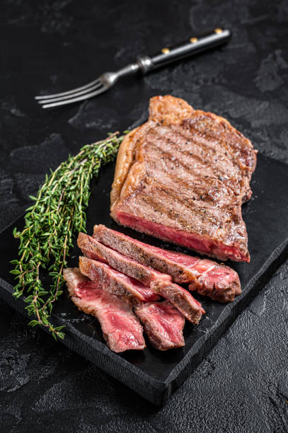 istock Griiled on BBQ sliced Striploin marbled beef meat steak. Black background. Top view 1454799369