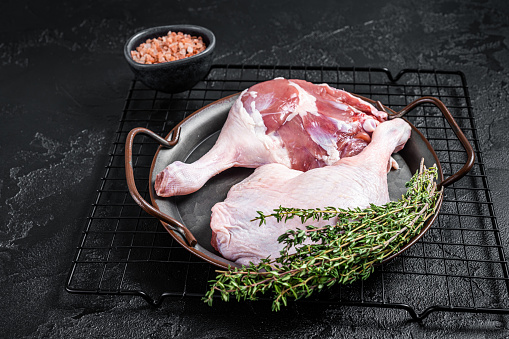 Raw Free range duck legs in a steel tray with thyme. Black background. Top view.
