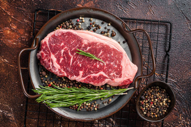 Raw New York or striploin beef meat steak with rosemary and pepper. Dark background. Top view Raw New York or striploin beef meat steak with rosemary and pepper. Dark background. Top view. marbled meat stock pictures, royalty-free photos & images