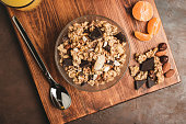 Granola cereal oatmeal with chocolate, fruist and nuts in a bowl on dark wooden board, top view