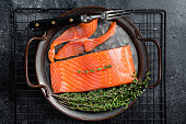 Slices of lightly salted salmon with thyme in a steel tray. Black background. Top view