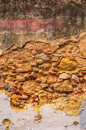 Fragment of an old brick wall with peeling cement plaster