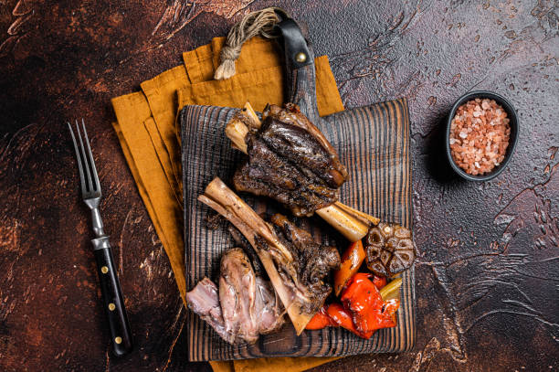 istock Traditionally slow cooked Leg of Lamb or Lamb Shank with vegetables on a cutting board. Dark background. Top view 1454801890