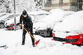 Young Man is Cleaning a Snow with Shovel in Front of a Car.