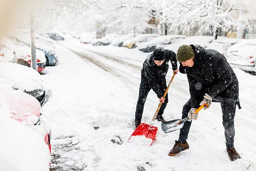 A Friends with Snow Shovel is Shoveling a Snow in Front of Car During a Cold Snowy Winter Day.