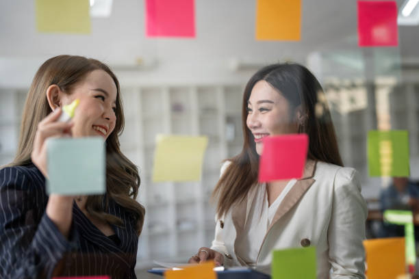 istock Two young  businesswoman creative team using post it notes in glass wall to writing strategy business plan to development grow to success. 1454804036