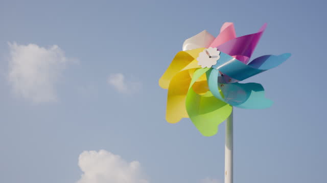 Colorful handmade windmills are spinning in the wind against a bright blue sky background with clouds.