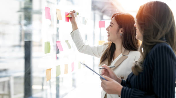 istock Young  businesswoman creative team using post it notes in glass wall to writing strategy business plan to development grow to success. 1454805403