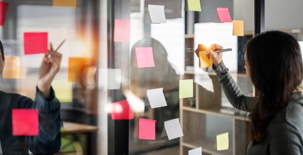 istock Team or staff discussing with sticky notes a schedule on glass wall for future project together, innovation and vision business meeting in a modern office,  working on a business marketing strategy. 1454805512