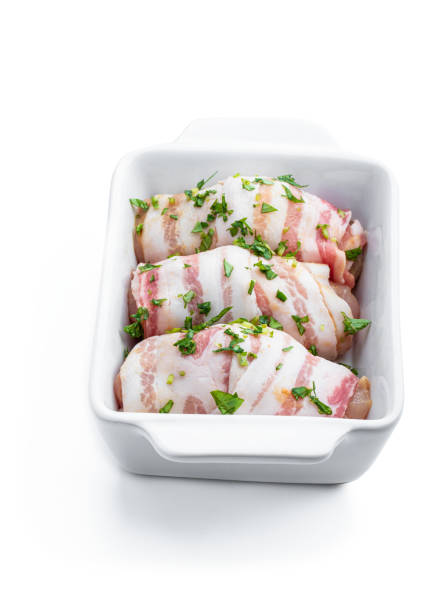 istock Raw Chicken breasts wrapped in bacon in white dish isolated on white. Ready to cook 1454806250