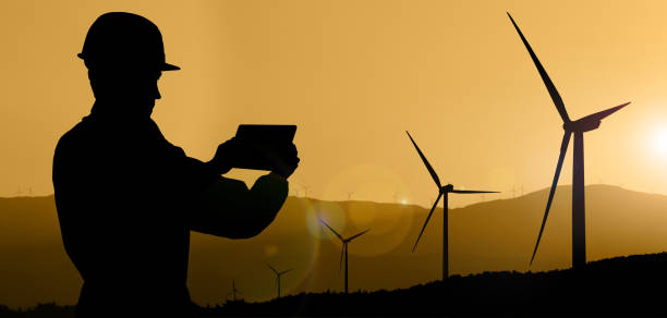 istock Silhouette of engineer with tablet computer and wind turbines 1454806303