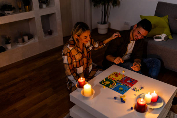 durante una crisi energetica, un uomo e una donna stanno giocando a un gioco di ludo al buio con candele accese. - crisis house burning color image foto e immagini stock