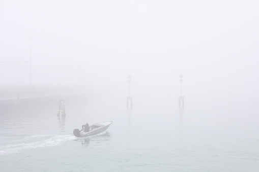 Daily life in Venice - Italy. Venetian on his motorboat in the Venetian lagoon on a foggy day. In the background the Ponte della Libertà (Liberty Bridge).
