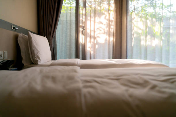 美容室には清潔な白い枕とベッドシーツが付いたベッドメイドアップ。クローズ アップ。日光の下でレンズの才能。装飾的な枕付きの新しいベッド掛け布団のクローズアップ、ステージング - bedroom hotel hotel room inn ストックフォトと画像
