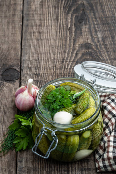 istock Pickled cucumbers in glass jar on wooden table 1454816783