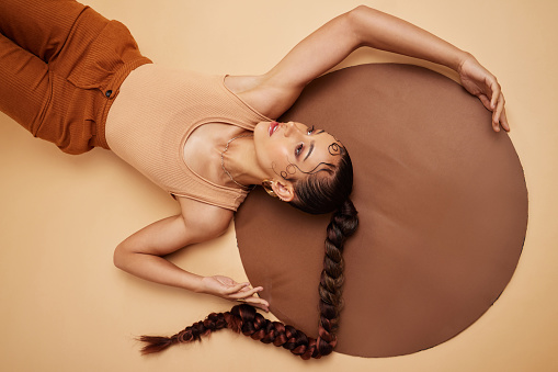 Creative, art and beauty with a model woman lying in studio on a beige background with a circle prop from above. Fashion, design and artistic with an attractive young female on the ground or floor