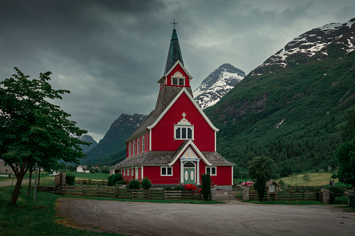 Red wooden church of Olden in the Nordfjord fjord in summer in Norway, moody atmosphere in the mountains and sky