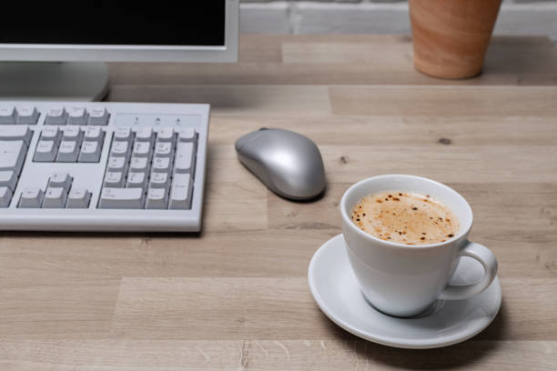 Blank screen computer monitor on working desk with coffee cup and vase