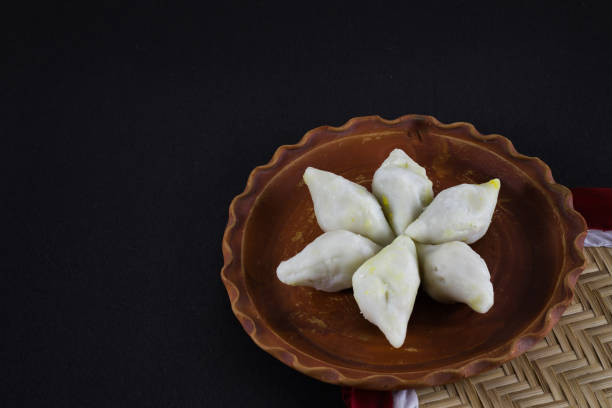 istock makar sangkranti or poush sangkranti celebration with puli pithe or bengali rice flour dumplings with coconut fillings served on a clay plate with jaggery. shot against black background. 1454829762