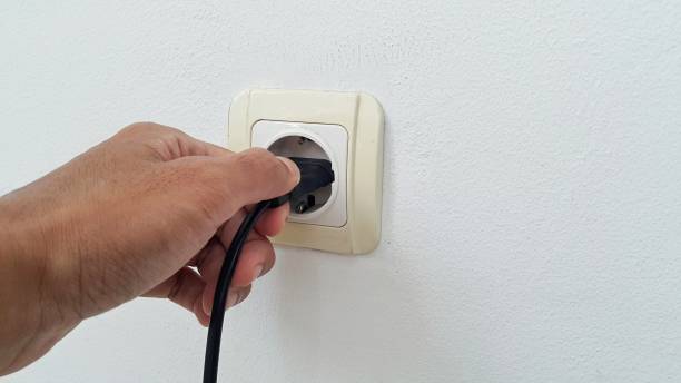 istock Hand plugging in an electric cord into a white plastic socket on white wall 1454830337