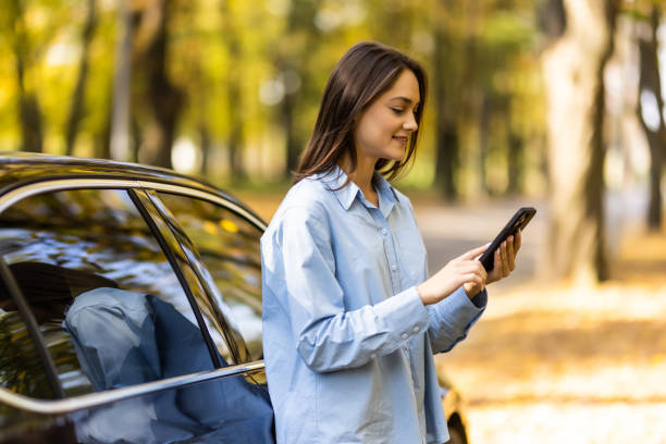 istock Successful smiling attractive woman is using her smart phone while standing near modern car outdoors 1454830409