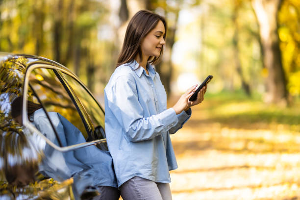 istock Successful smiling attractive woman is using her smart phone while standing near modern car outdoors 1454830714