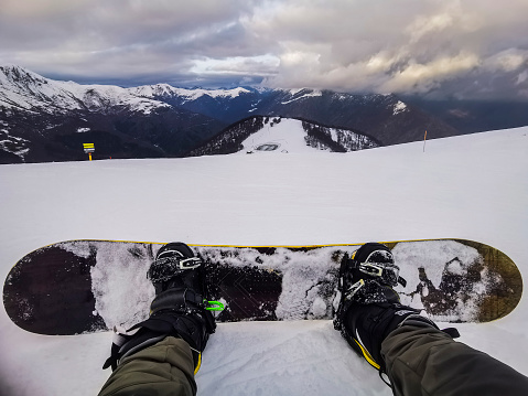 People in winter mountains holiday vacation. Pov of legs and snowboard with landscape scenic view. Rider enjoying panorama and sky. One man resting in ski facilites. Active outdoor lifestyle