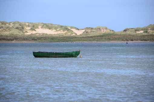 Single rowing boats of different colours with the sand dunes at Newburgh beach, Aberdeenshire, Scotland in the background.