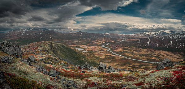 Landscape panorama with river Leirungsae with snow covered mountains in Jotunheimen National Park in Norway from above, dark clouds in sky