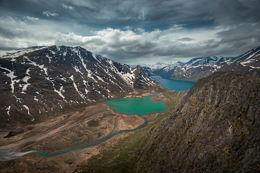 Turquoise and blue lakes in mountain landscape from above the hike to Knutshoe summit in Jotunheimen National Park in Norway, mountains of Besseggen in background, cloudy sky