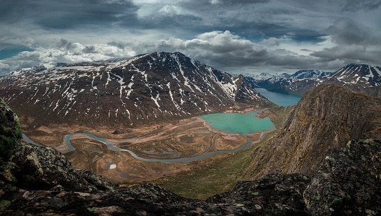 Turquoise and blue lakes in mountain landscape from above the hike to Knutshoe summit in Jotunheimen National Park in Norway, mountains of Besseggen in background, cloudy sky