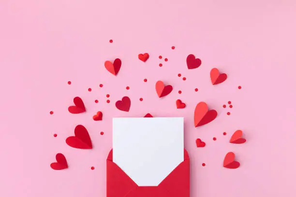 Photo of Saint Valentine day holiday background with envelope, paper card and various red hearts for love romantic message flat lay.