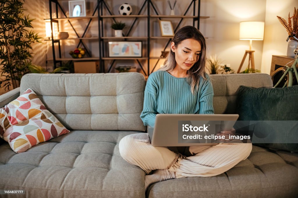 Woman using Laptop at home Photo of a young woman using her laptop at night on sofa People Stock Photo