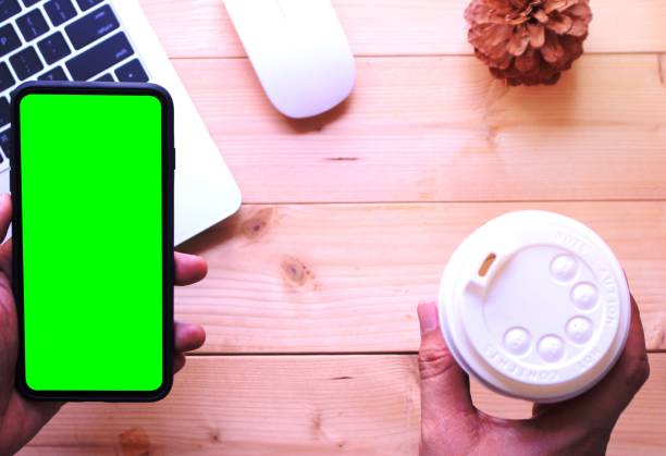 istock business man holding green screen smartphone with coffee cup on office table desk background 1454843816