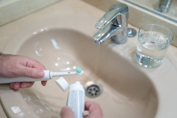 istock Man's hands pouring toothpaste into an electric toothbrush in the bathroom sink. 1454845198