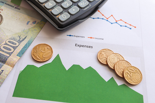 Cost of living and expenses. Reduce expense with a drop in income. South African currency the Rand with graphs depicting expenses and a calculator in the background