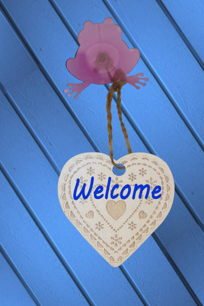 istock Welcome marked on a wooden heart fixed to a facade by a frog-shaped suction cup 1454850548